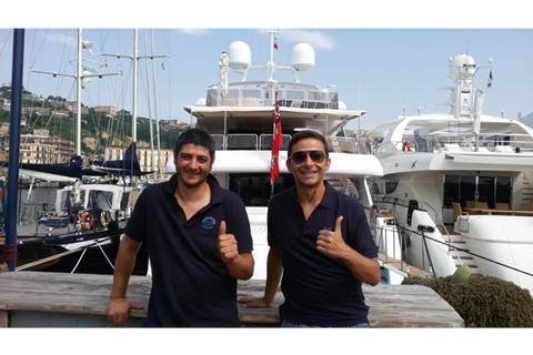 Two men standing thumbs up in front of a superyacht.