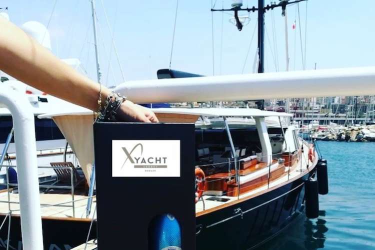 Champagne bottle in a XYacht branded package on a dock with a yacht in the background
